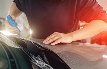 Detailer worker sprays by soap sud and wrap PPF or car protection film on vehicle hood